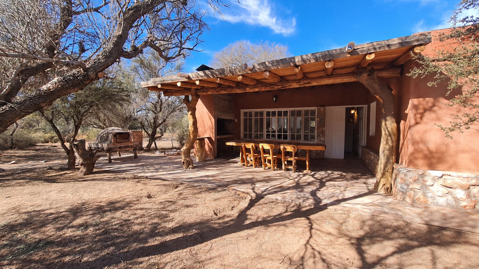 Exterior de Cabañas Ischigualasto con galería, horno de barro y monte nativo